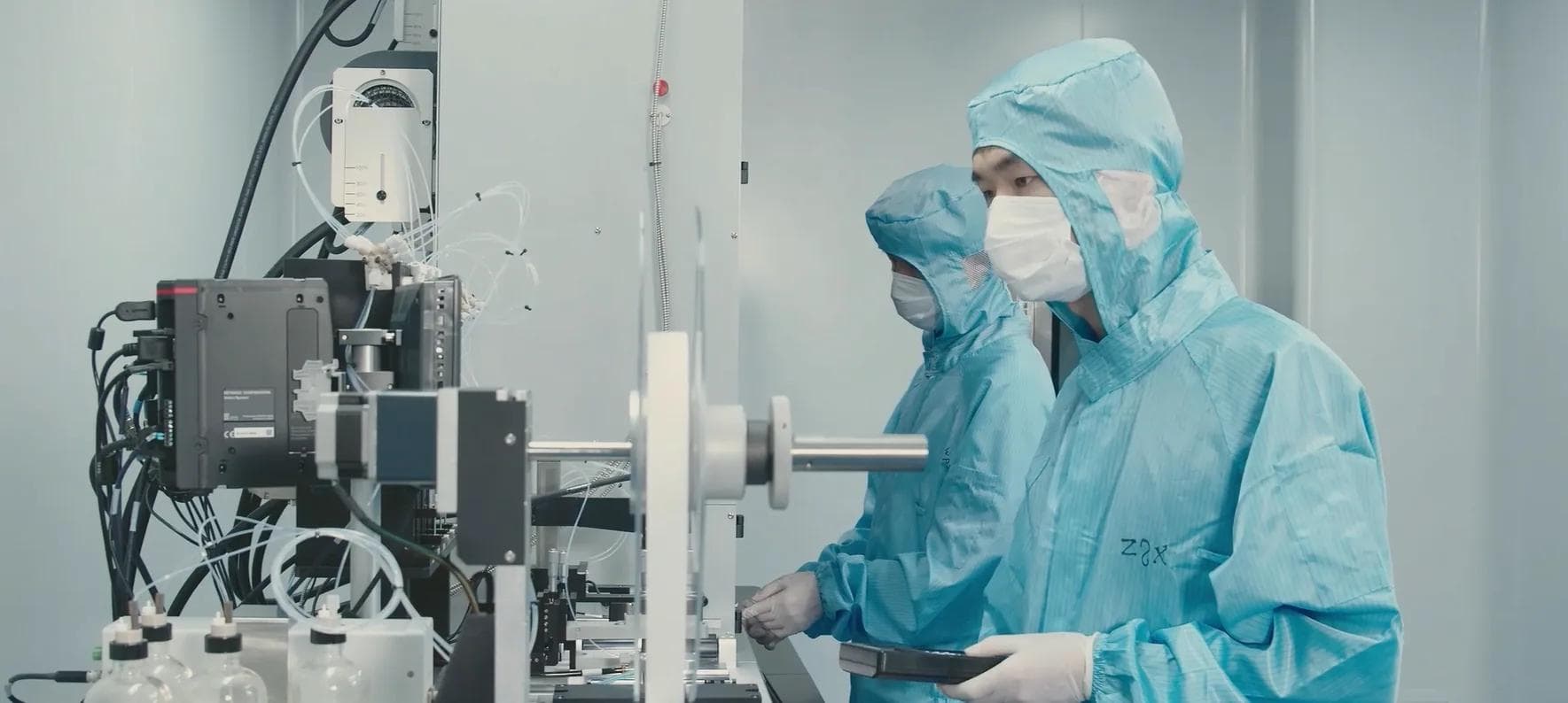 Two technicians in protective clothing working at an instrument line in a controlled laboratory environment